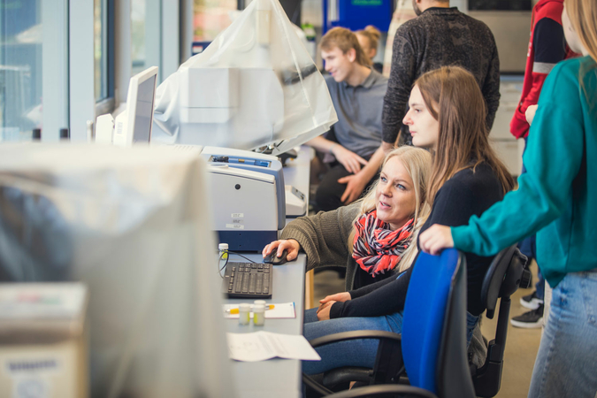 Eine Schülerin sitzt an einem Computer, eine Frau kniet neben ihr und bedient die Maus.