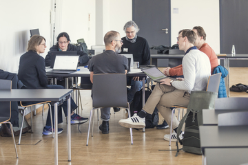 Das Bild zeigt Personen, die mit Laptops zusammensitzen.